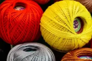 Four balls of cotton crochet thread, in red, yellow, orange, and silver.