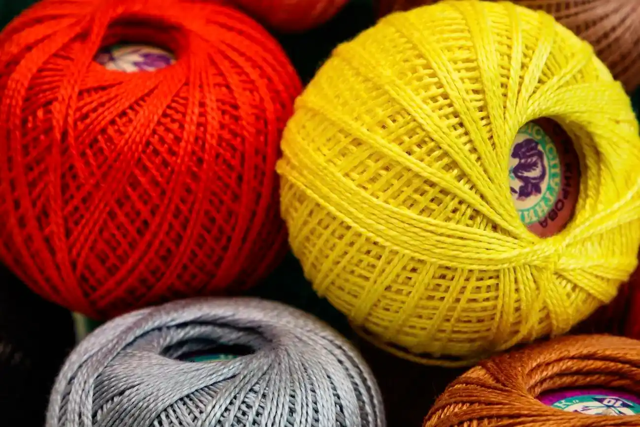 Four balls of cotton crochet thread, in red, yellow, orange, and silver.