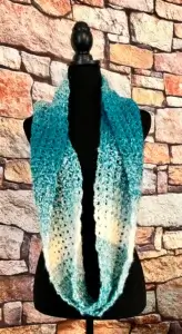 A white and teal crochet infinity scarf is displayed on a dressmaker's form.